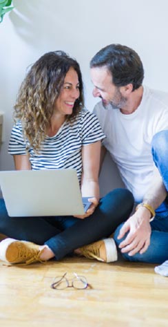 Middle-aged couple sitting together with laptop smiling at each other
