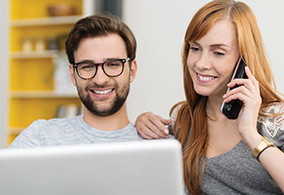 Couple sitting together while looking at laptop and talking on home phone