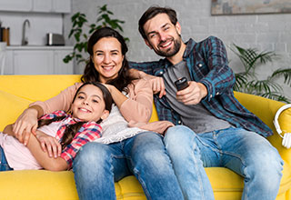 Family sitting on couch pointing TV remote and looking at camera