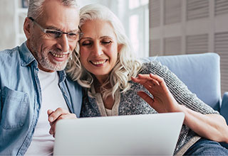 Elderly couple sitting on couch looking at laptop together