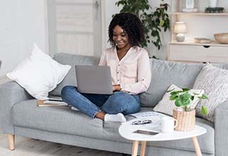 Woman sitting on couch using laptop and smiling