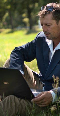 Man in business-casual attire sitting on grass with laptop